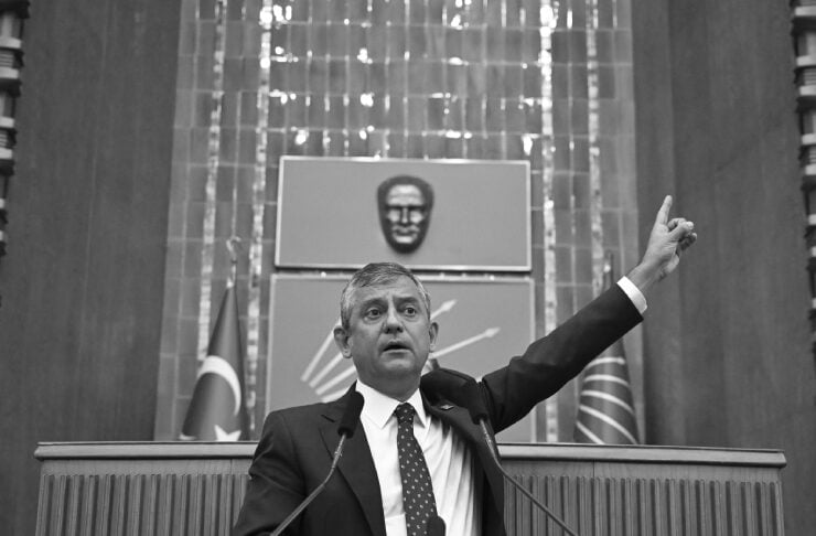 Male politician speaks at a lectern, raises his right arm, CHP banner in front.