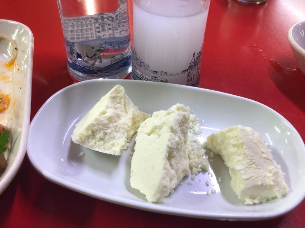 Three irregular chunks of white cheese on a white oval plate atop a red table.