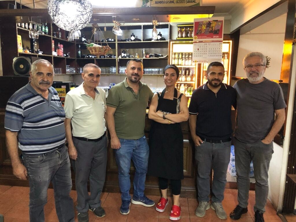 Six staff members, five men and one woman, stand behind a bar counter in a cafe, posing for a group photo.