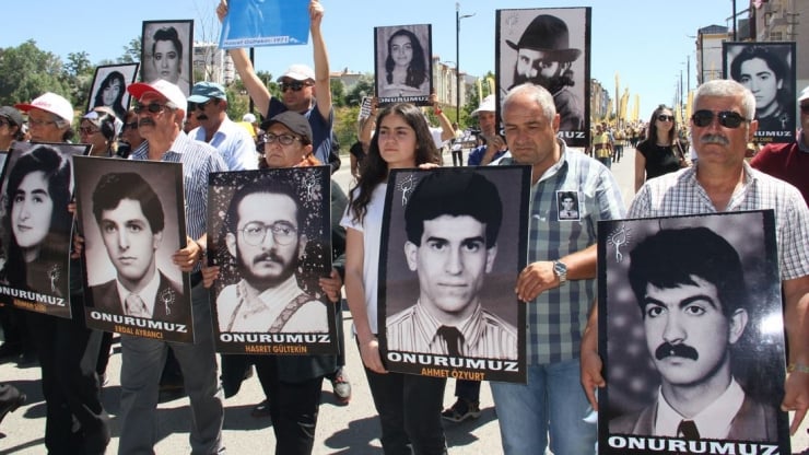 Group of protesters marching in a street, holding large portrait posters of men and women with the word 'ONURUMUZ' visible on several signs.