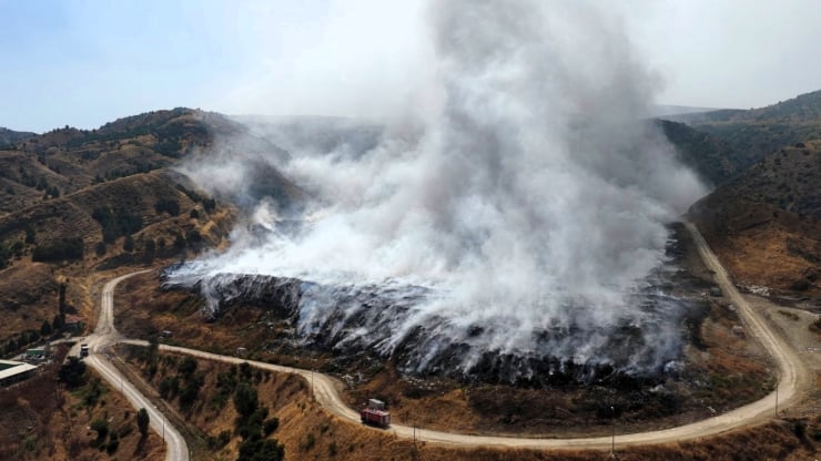 Hillside with active fire and thick smoke rising, surrounded by a winding dirt road from an aerial view