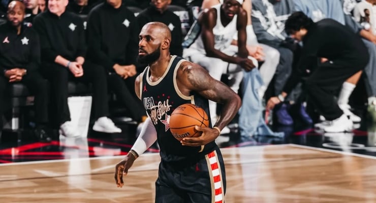 Basketball player in a dark USA jersey dribbles the ball down the court with spectators watching from the sidelines.