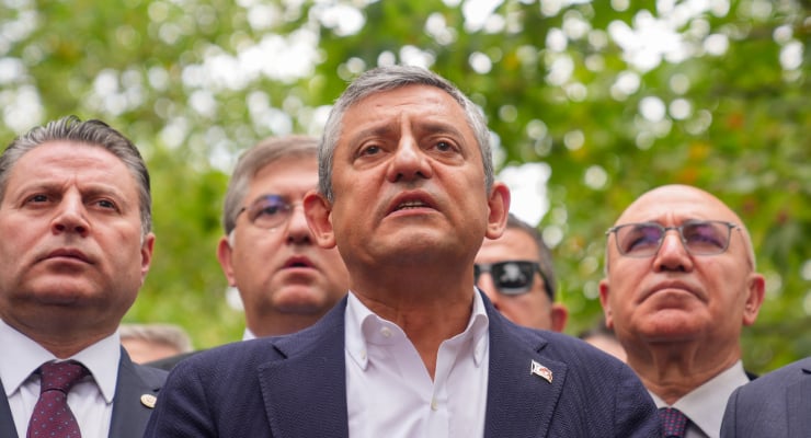 Group of men in suits looking upward at something off-camera at an outdoor event; central man in white shirt and blazer wearing a small flag pin.