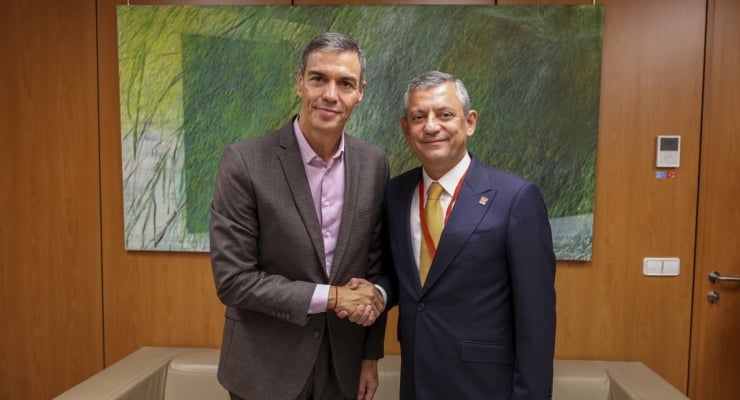 Two men in suits shake hands in a wood-paneled room with a green abstract painting behind them.