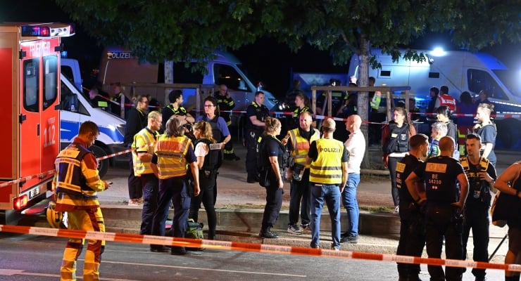 Nighttime emergency scene with police, paramedics, and ambulances behind red-and-white tape on a cordoned street.