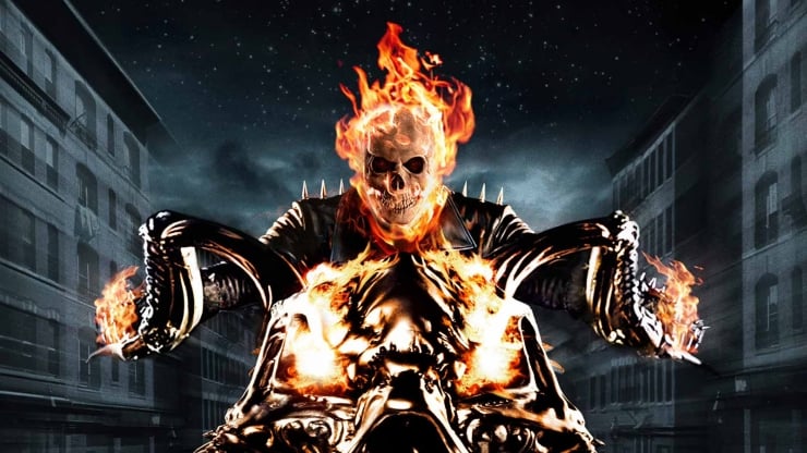 Flaming skull-faced figure in a black leather jacket stands with arms outstretched in a dark city alley at night, flames rising from its body.