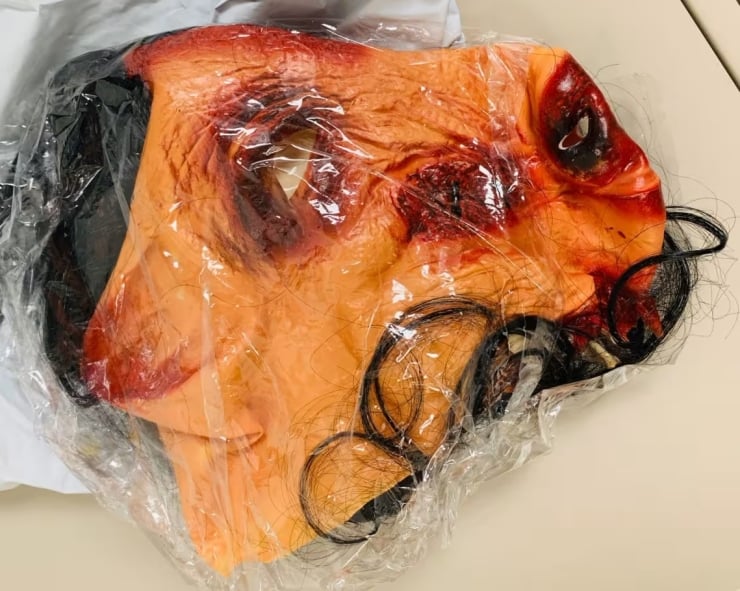 Life-size horror prop head with burned facial injuries wrapped in clear plastic, used as a prop or display piece.