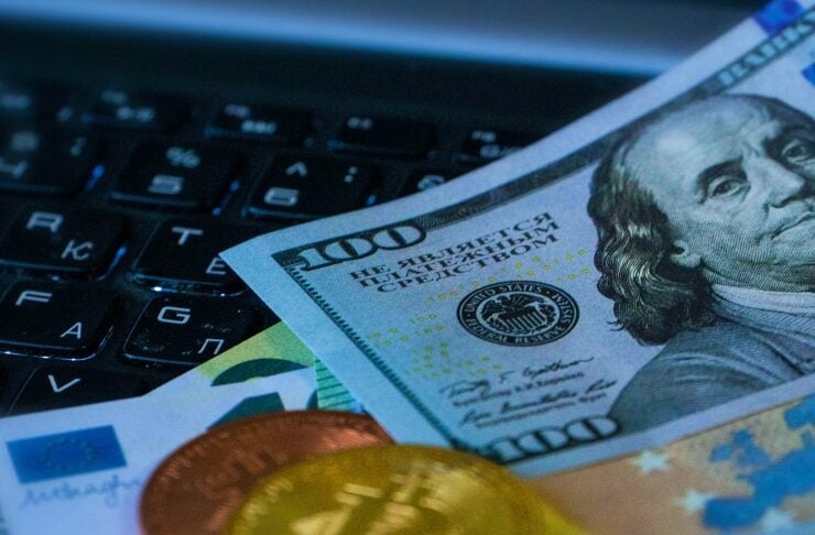 Close-up of a 100-dollar bill and coins resting on a dark laptop keyboard, suggesting online finance or digital payment.