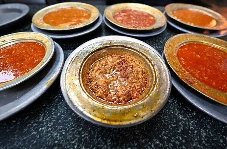 Assorted metal bowls with different curry sauces on a dark countertop, center bowl showing a thick brown gravy.
