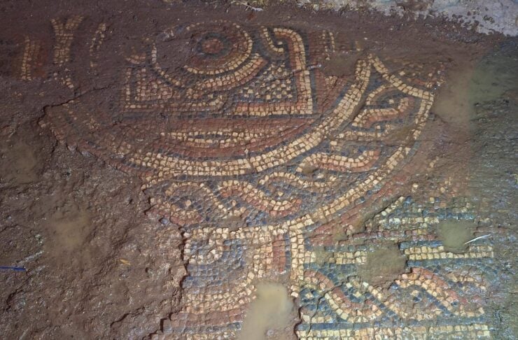 Mosaic tile design embedded in muddy ground, featuring circular and geometric patterns.