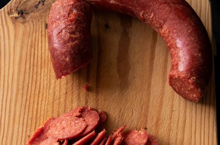 Sliced salami arranged on a wooden cutting board with a curved piece of sausage above it