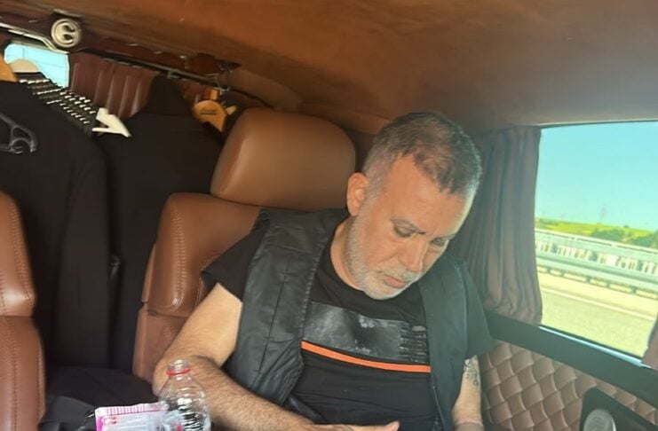 Man sits in a brown leather car interior, reviewing papers on his lap with a water bottle and a folder nearby on the seat.