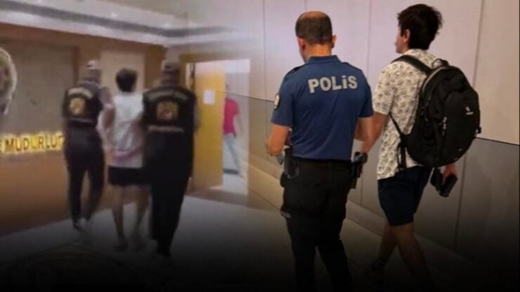 Policeman in blue uniform labeled POLIS escorts a civilian down a hallway with other people walking ahead.