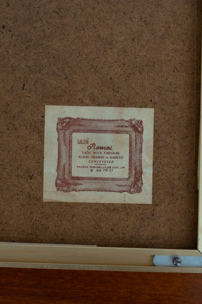 Small vintage flyer pasted on a brown corkboard, featuring an ornate framed label with Turkish text (Galerı Remzi).