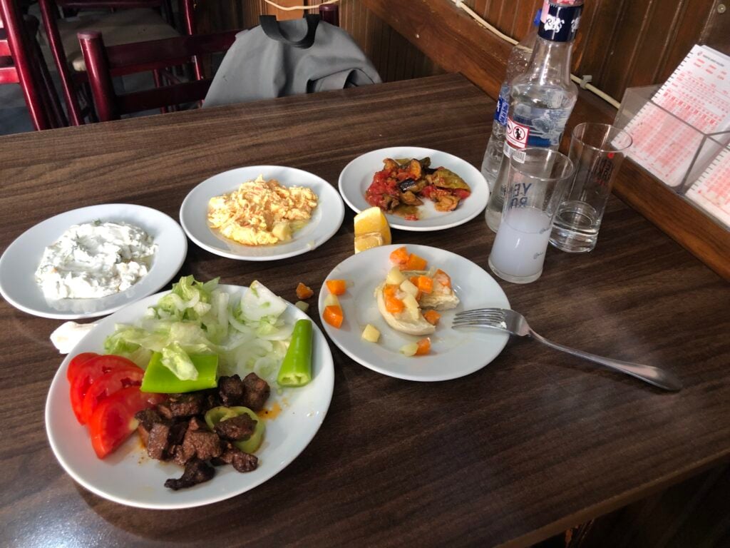 Assorted dishes on a wood table: beef with peppers, potato salad, scrambled eggs, and mixed vegetables with tomato and lettuce slices.