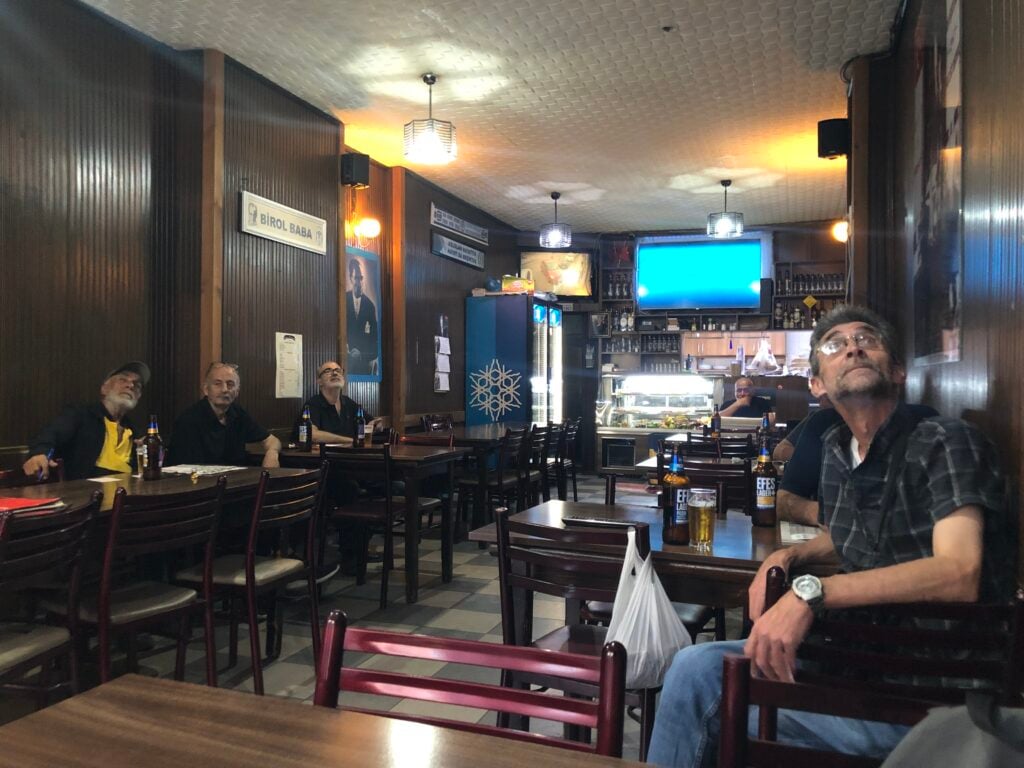Interior of a casual dining bar with patrons sitting at tables and bottles on the counter; warm lighting and dark wood paneling.