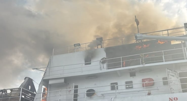 White ship with smoking flames on the upper deck and security railings, suggesting a fire onboard.