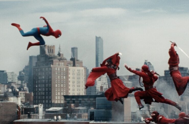 Spider-Man leaps between rooftops as several red-clad fighters jump through the air over a city skyline.