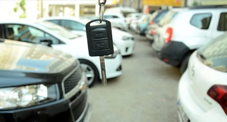Car key hanging from a lanyard in the foreground with a row of parked cars in a dealership lot behind it