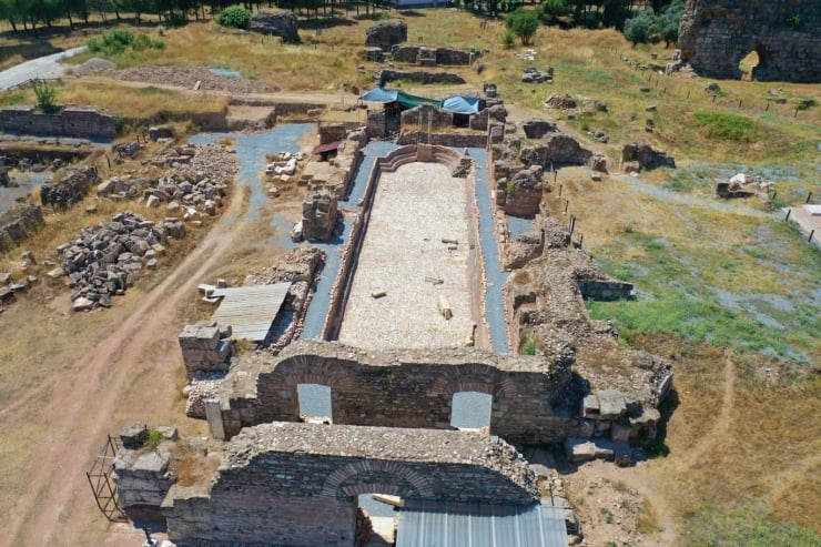 Aerial view of ancient stone ruins with a long rectangular central courtyard and crumbling walls surrounded by dry grassy terrain.