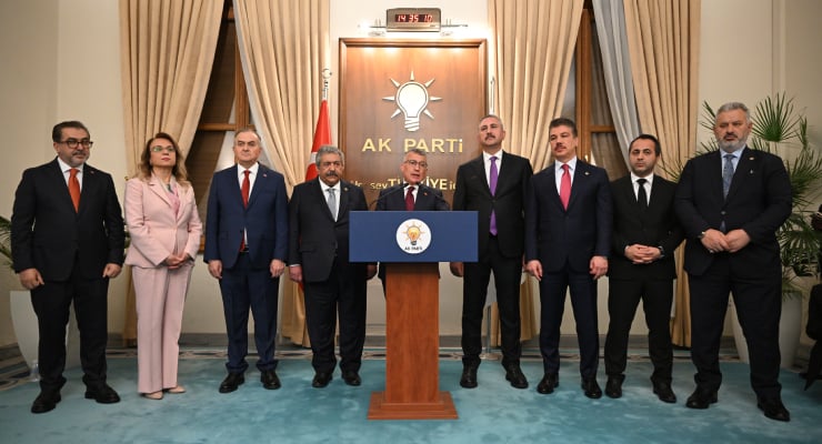 Group of eight people in suits standing behind a podium with the AK Parti emblem in a formal room.