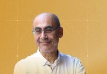 Smiling middle-aged man with glasses in a white shirt, arms crossed, against an orange background with circular design elements.