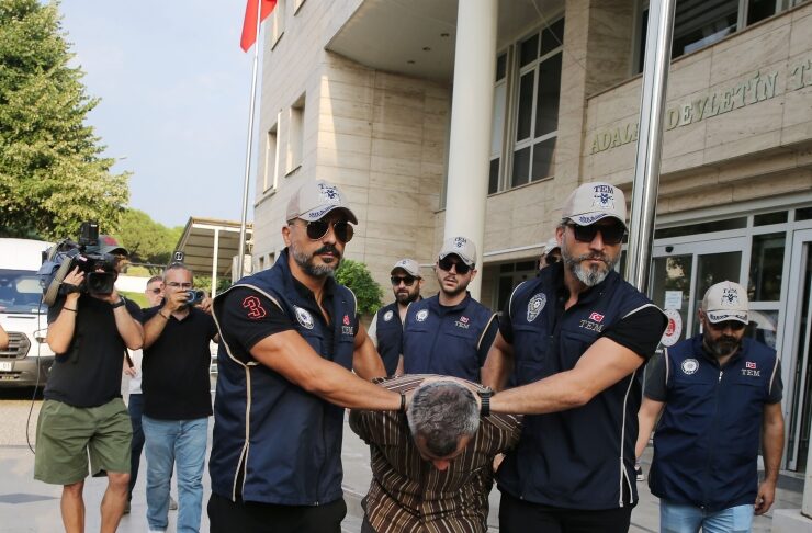 Group of uniformed men restrain a man outside a government building; photographers film nearby.