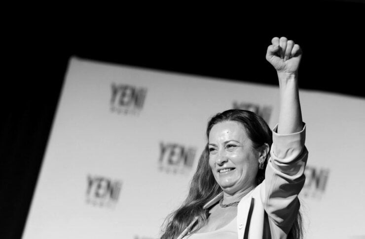 Woman on stage with long hair raises her right fist in the air in a celebratory gesture at a YEN event, with a branded backdrop behind her.