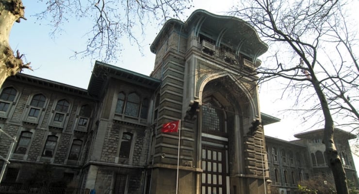 Historic stone building with an ornate archway entrance and a Turkish flag on a flagpole in front.