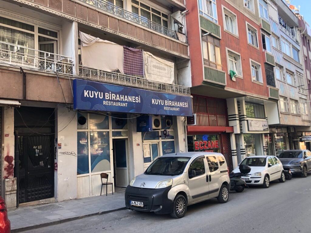 KUYU BIRAHANESI Restaurant sign on a street with parked vans and apartment buildings above.