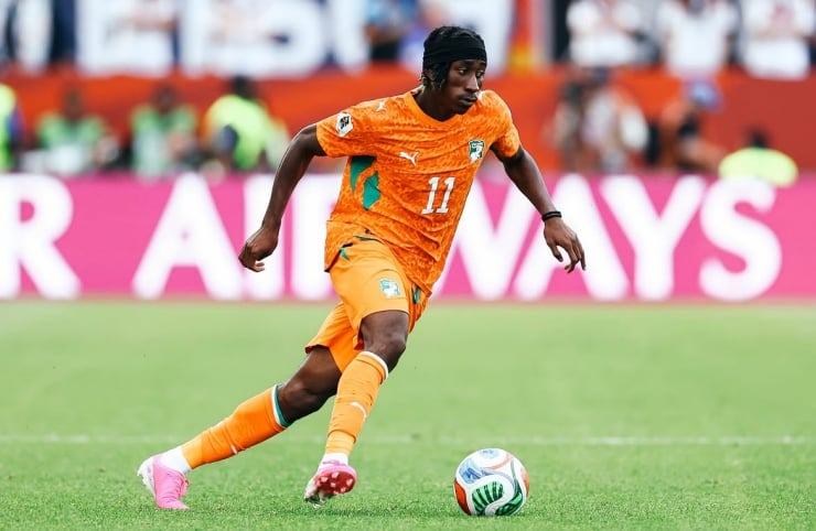 Soccer player in an orange kit with number 11 dribbling the ball on a green field during a match.