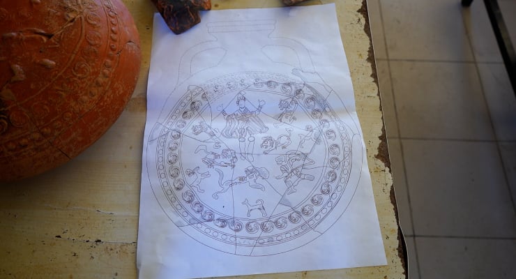 White sheet with a large circular mandala design on a wooden counter, a pumpkin visible to the left.