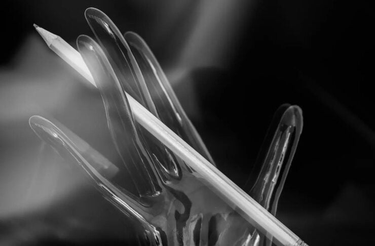 Black-and-white photo of a glass hand sculpture with a pencil resting diagonally across its fingers.
