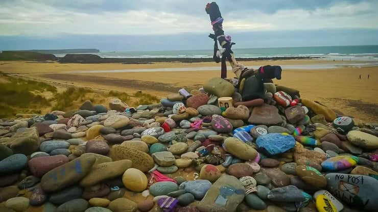 Colorful painted rocks forming a cairn with stuffed animals on a sandy beach, ocean in the background.