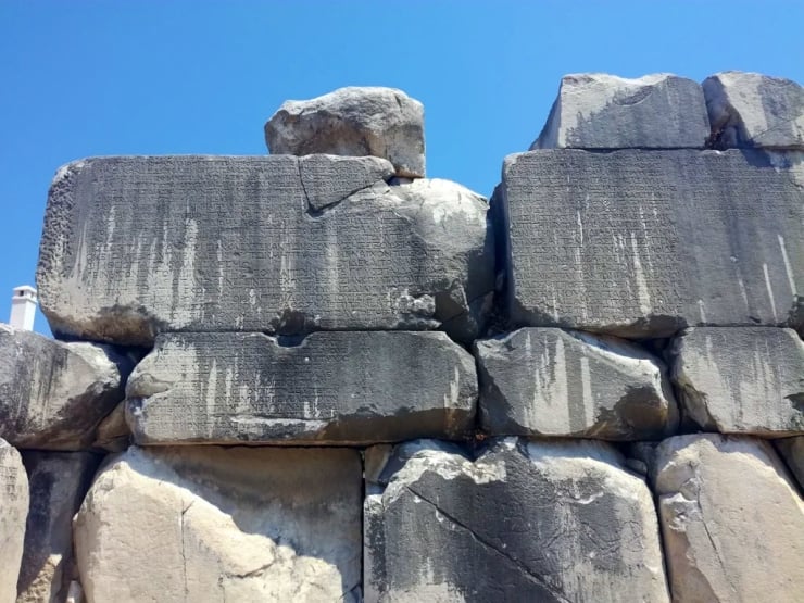 Rough gray stone wall made of huge rectangular blocks stacked under a clear blue sky.