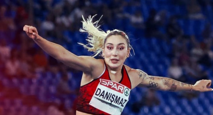 Turkish female long jumper in a red uniform with a bib reading DANIŞMAZ, arms outstretched mid-air during the jump.