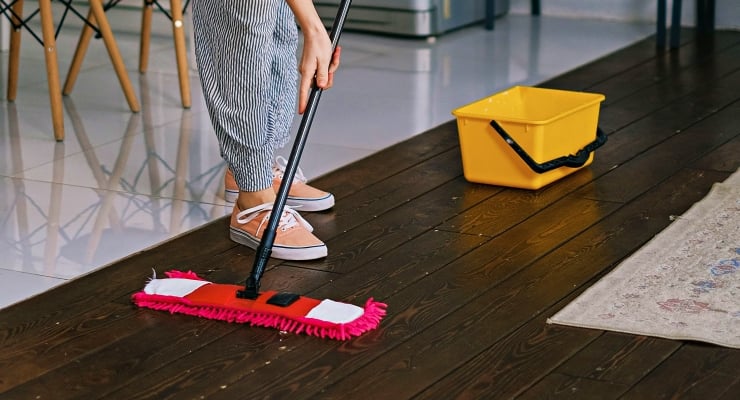 Person mopping a dark wooden floor with a red mop; a yellow bucket sits nearby.