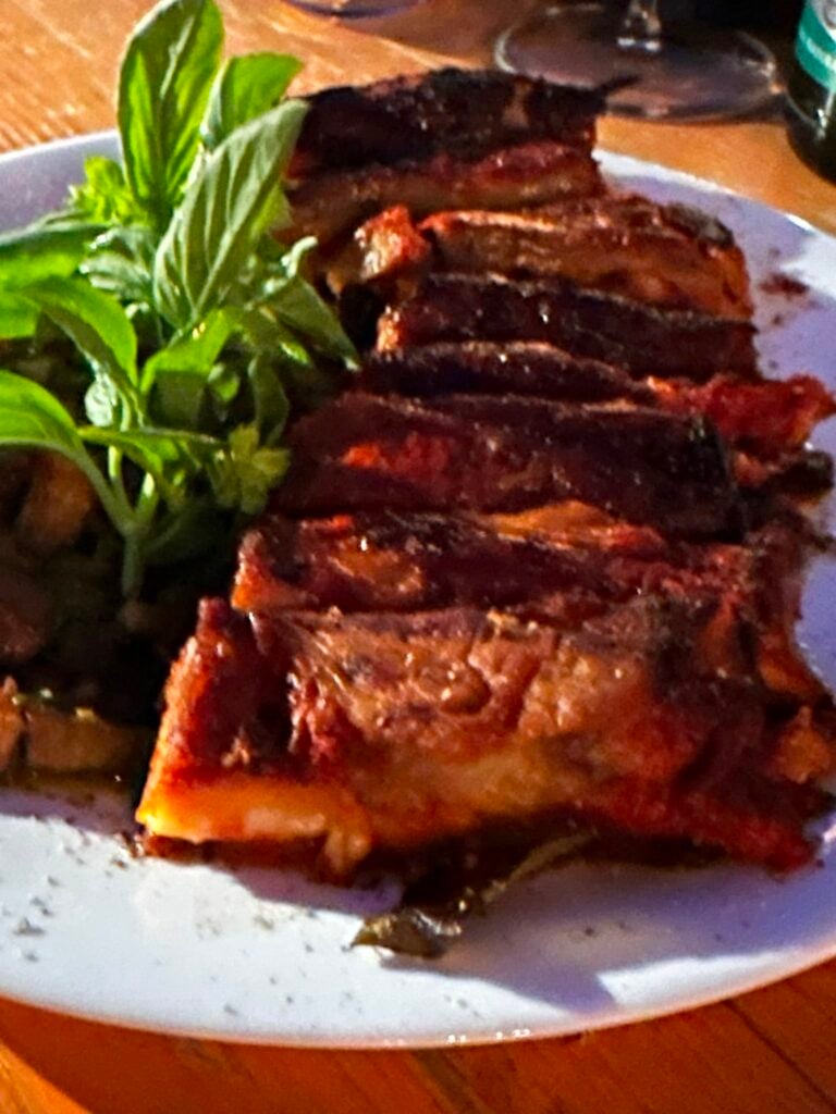 Sliced grilled steak arranged on a white plate with a sprig of fresh greens on the side.