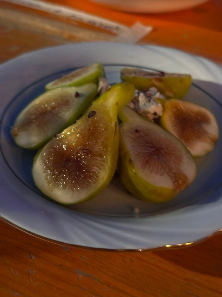 Halved green figs scattered on a white plate, with a little crumbly cheese nearby.