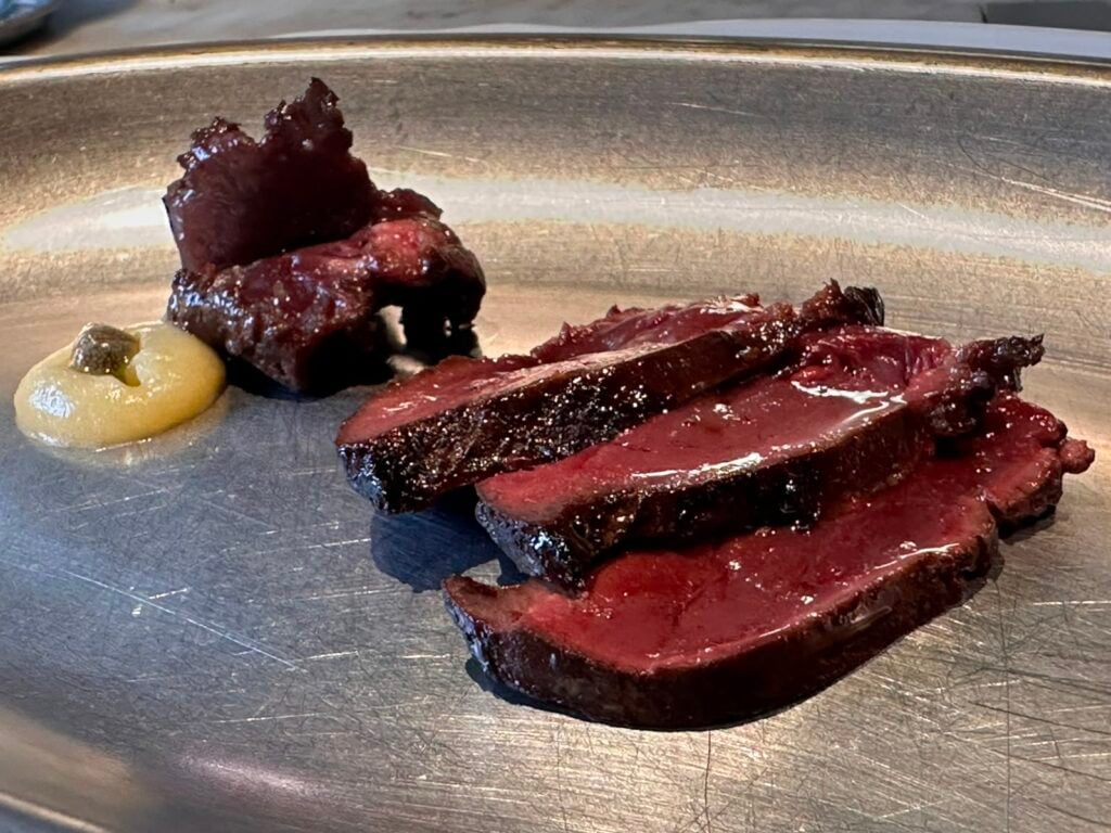 Slices of medium-rare beef steak arranged on a metal plate, with a small dab of mustard on the side