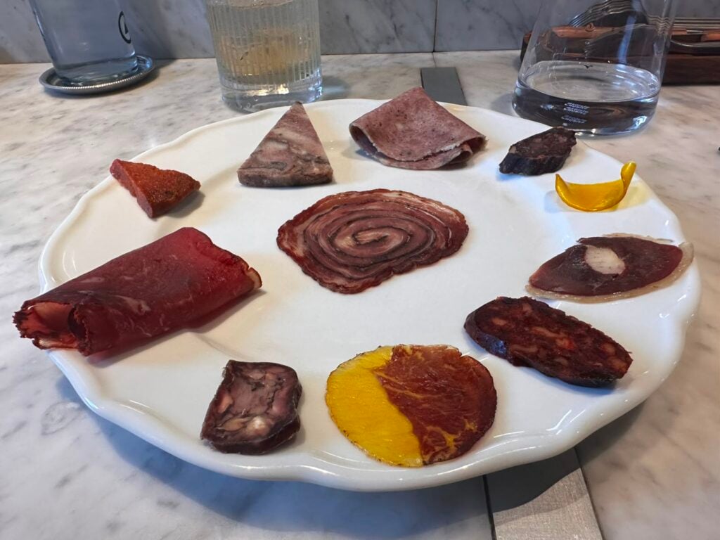Assorted cured meats arranged in a circle on a white plate, with a spiral roast beef center.