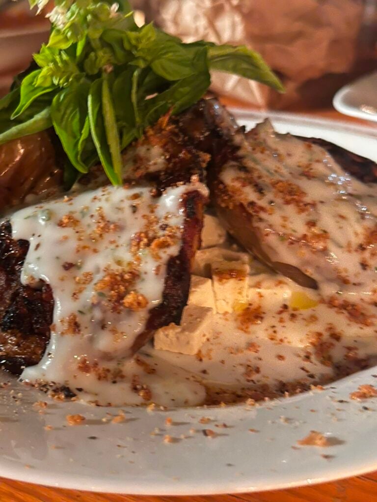 Sliced steak with creamy herb sauce, sprinkled with spices, and a green herb garnish on a white plate