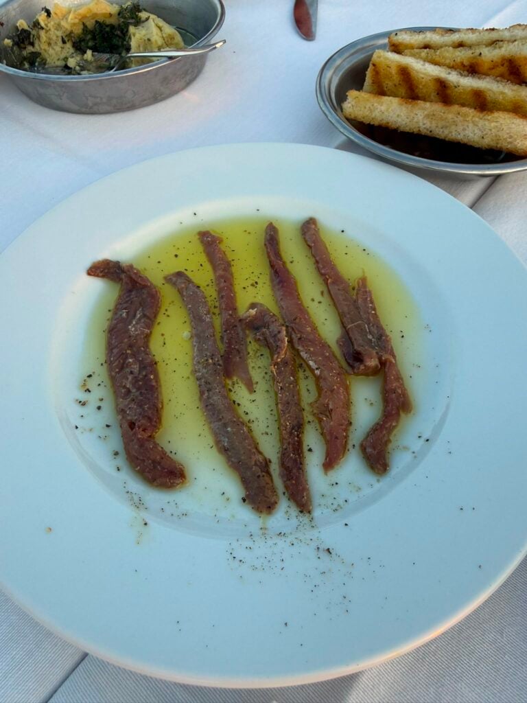 White plate with several thin slices of raw beef marinated in olive oil and sprinkled with cracked pepper.